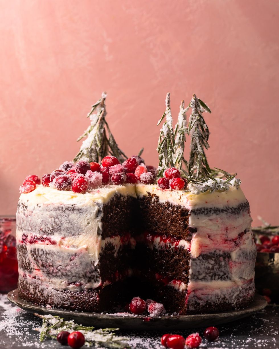 three layer chocolate cake with cranberry filling between the layers and mascarpone frosting covering the whole cake and sugared cranberries and rosemary on top for garnish