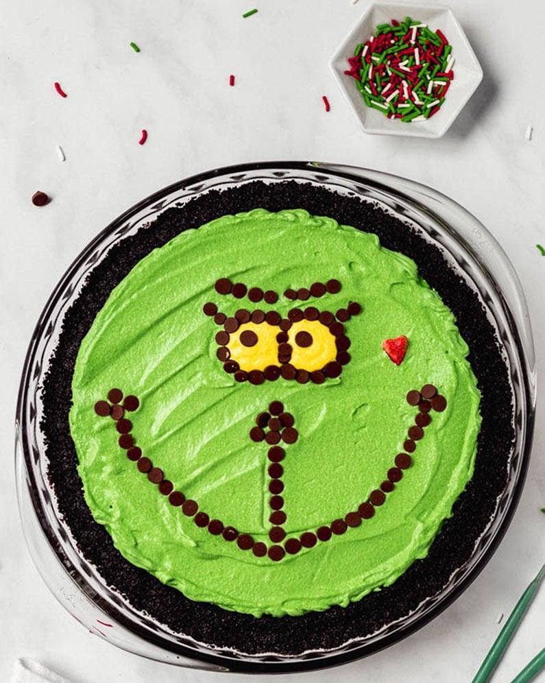 a green no bake cheese cake decorated with mini chocolate chips to create the face of the grinch on top