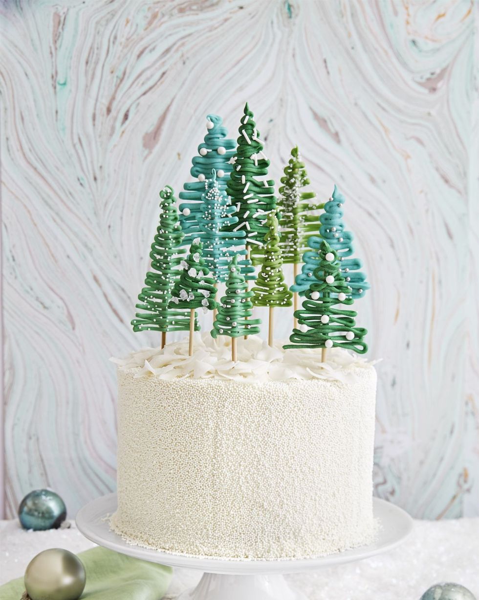 layer cake covered in white nonpareils with various sized and colored green candy pine trees sticking out of the top