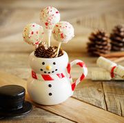 close up of peppermint cake pops sitting in snowman mug with party poppers and pine cone decorations for the holidays