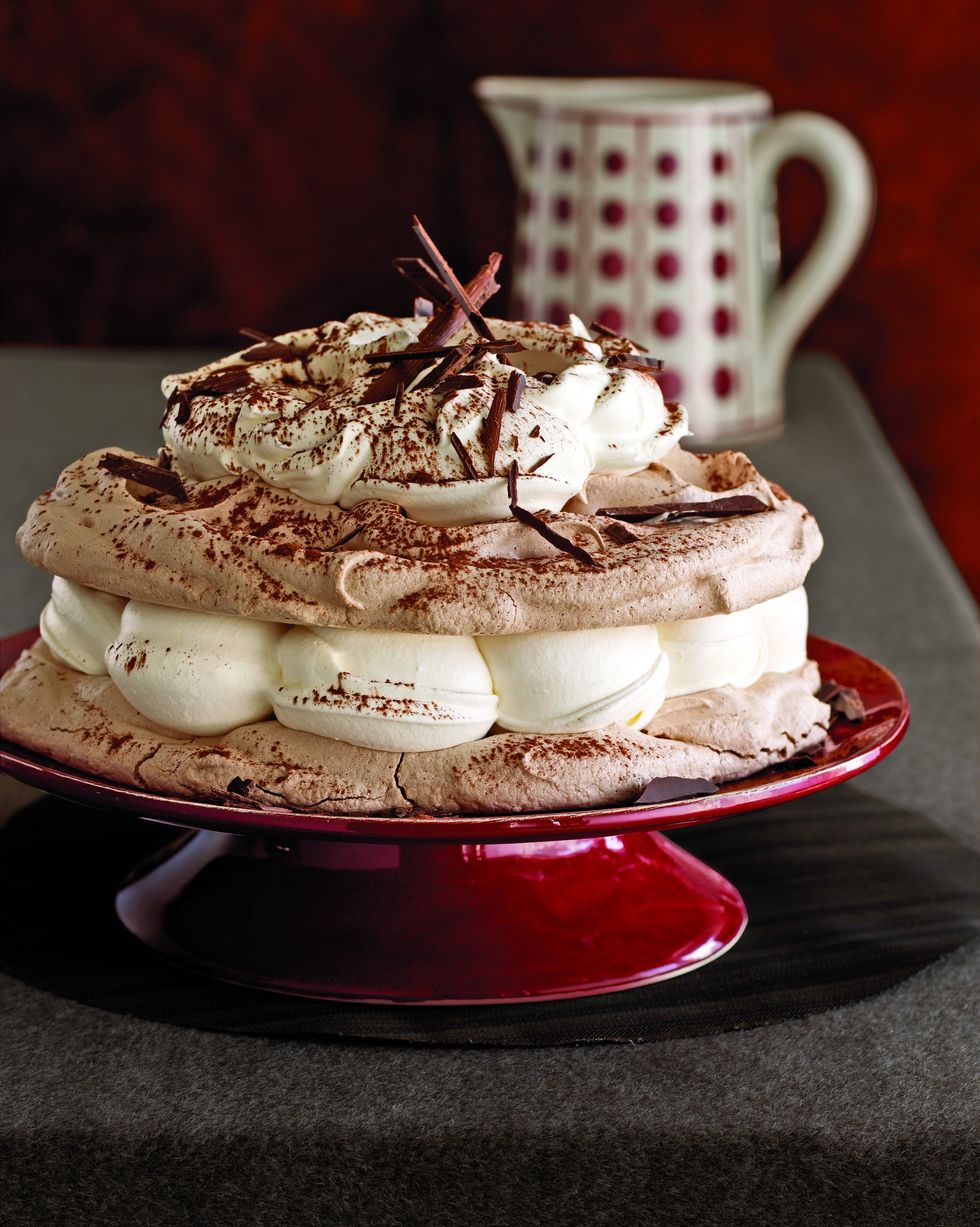hot chocolate meringue cake on a red cake stand and topped with whipped cream and shaved chocolate