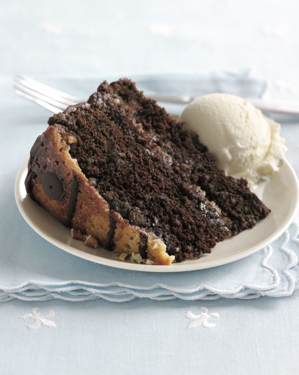 a slice of praline turtle cake on a white plate with a scoop of vanilla ice cream