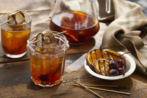 grilled orange old fashioned in glasses with ice and grilled orange slices and a toasted marshmallow on a toothpick for garnish