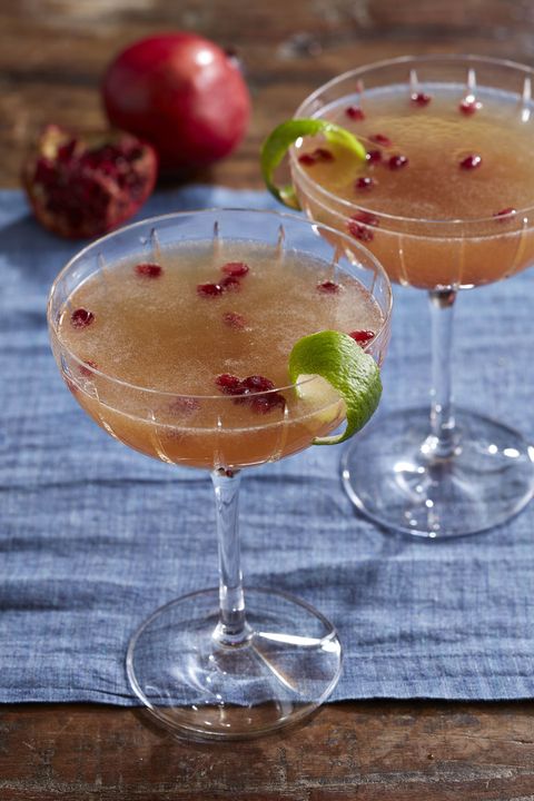 pomegranate french 75 in coup glasses with pomegranate seeds and a strip of lime peel as garnish