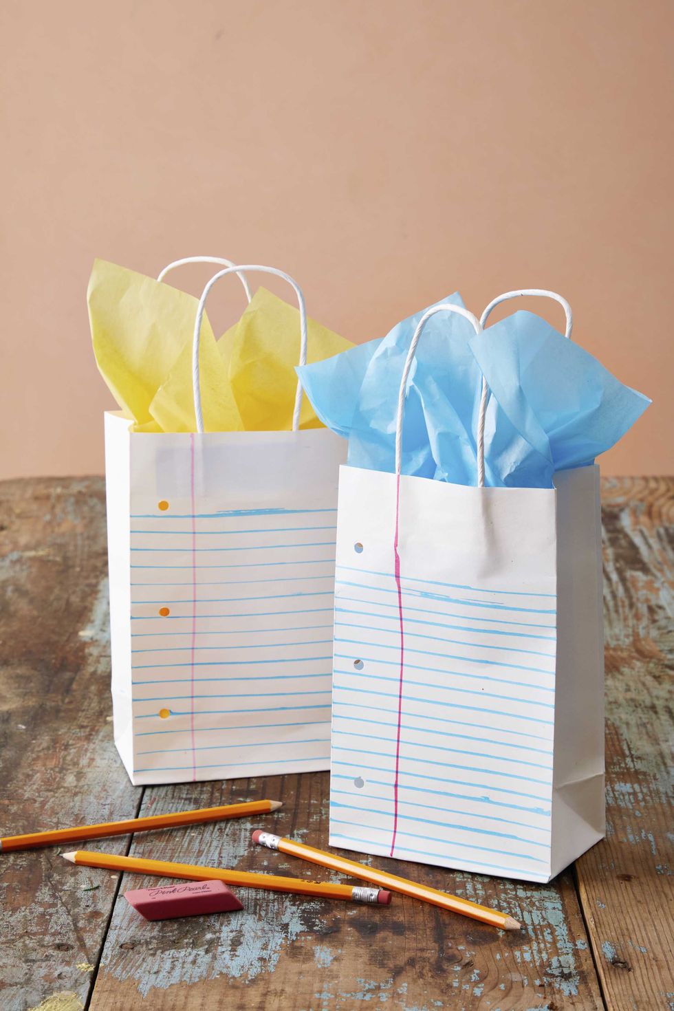 white paper gift bags decorated with pens and a hole punch to look like ruled school paper