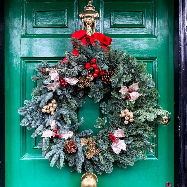 christmas mood festive christmasy themed winter natural wreath on a green wooden door decorated with red bow, berries, pine cones and  fir tree