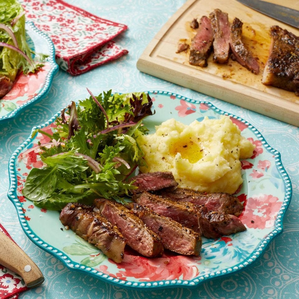 pan fried rib eye with mashed potatoes and salad on floral plate