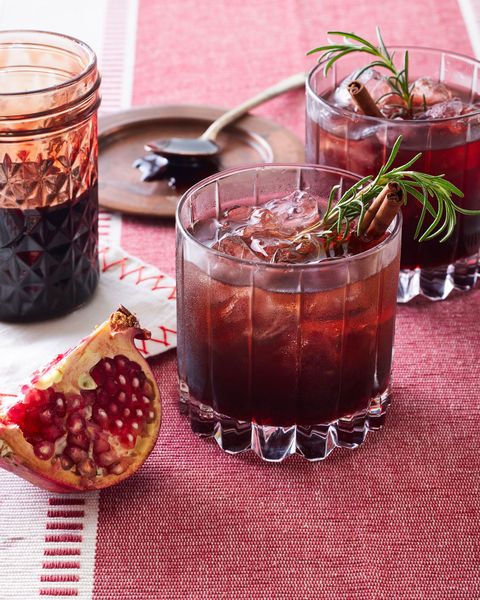 poinsettia cocktail in a glass with ice and garnished with a sprig of rosemary and a cinnamon stick