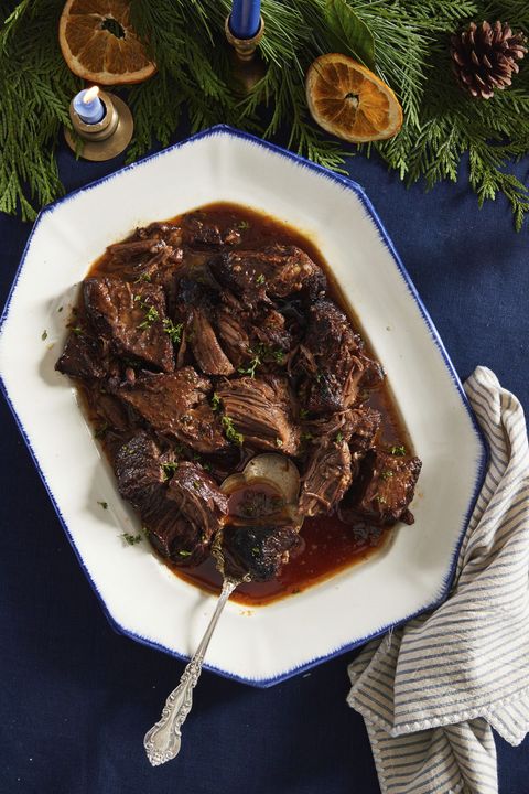 red wine braised short ribs in a white oval serving dish with a spoon