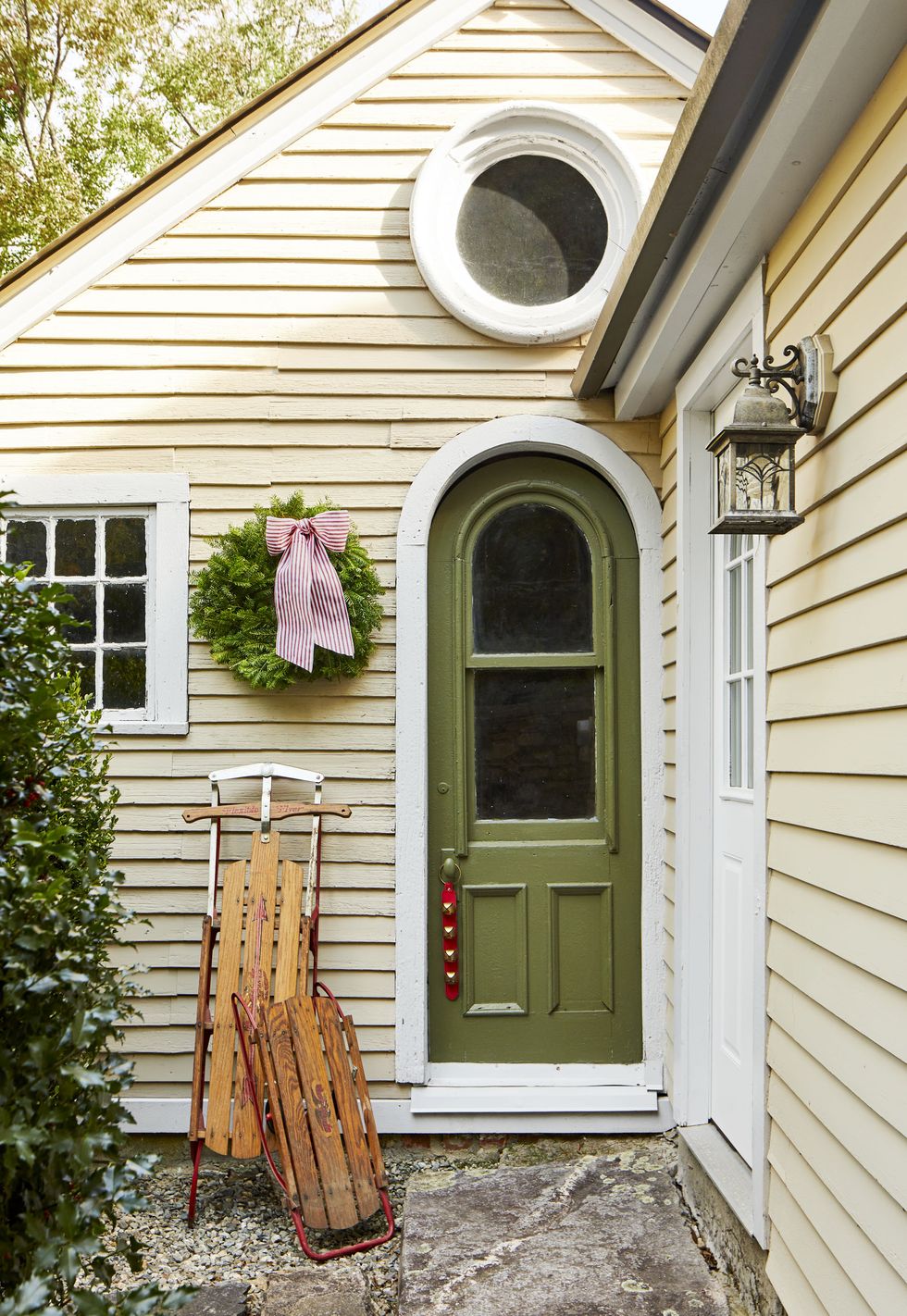 green front door with christmas bells hanging from the door knob and sleds leaned up against the house