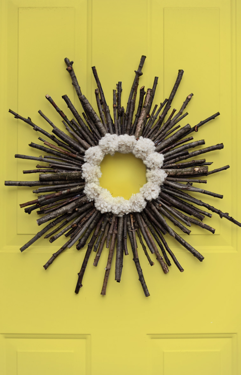 christmas door decorations, wreath made of twigs and white pom poms hanging on yellow door