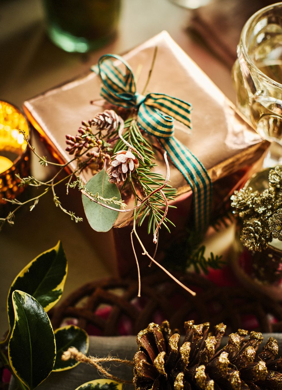 gift with rose gold wrapping paper tied with checked ribbon and a tiny corsage of twigs and cones brighten a tabletop with large gold sprayed cones