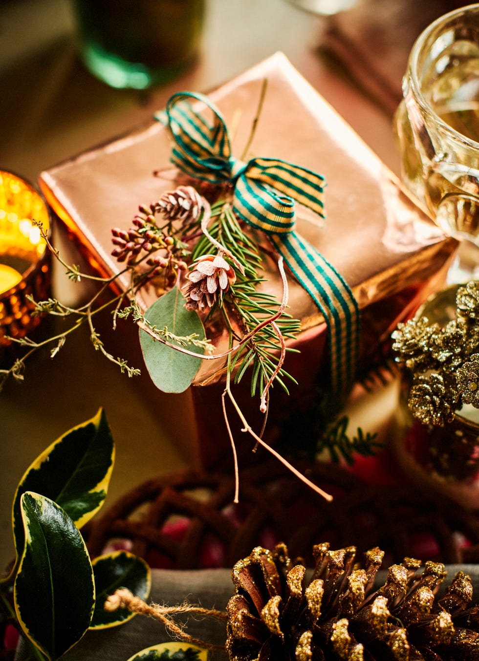 gift with rose gold wrapping paper tied with checked ribbon and a tiny corsage of twigs and cones brighten a tabletop with large gold sprayed cones