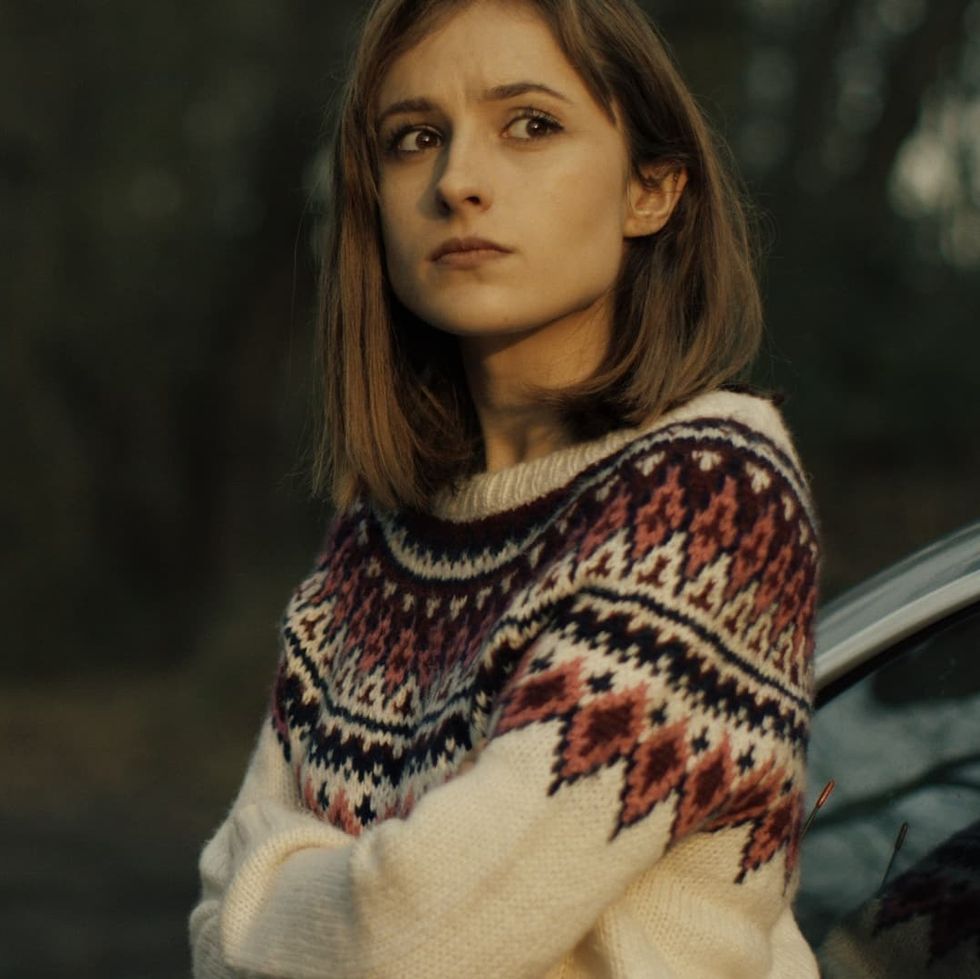 a woman wearing a warm sweater looks out into the distance in a scene from mother krampus