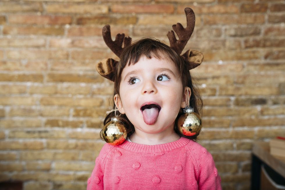 portrait of toddler girl sticking out tongue wearing reindeer antlers headband and christmas baubles