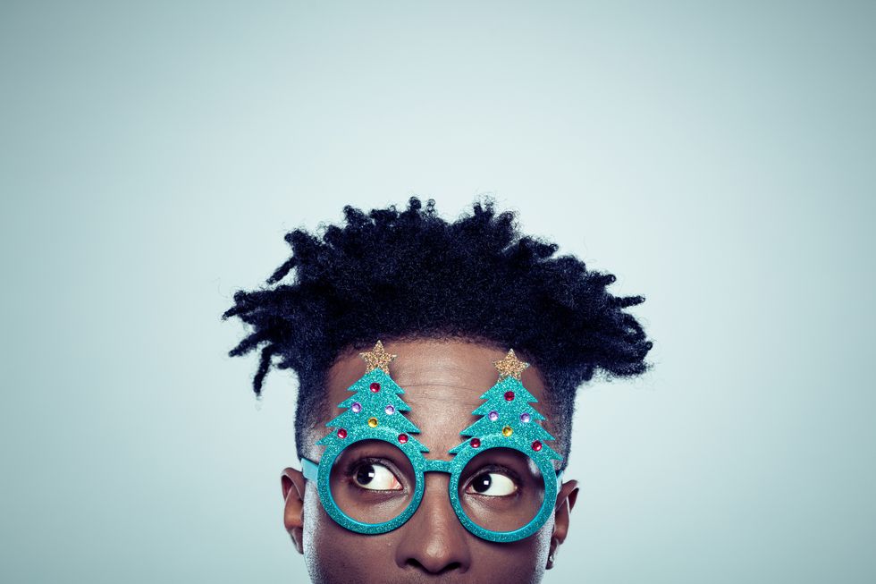 close up of african man wearing christmas tree shaped glasses looking away on gray background
