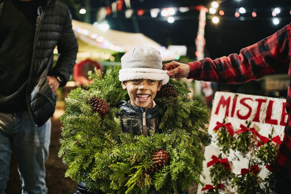 smiling boy wearing christmas wreath while shopping for tree with family