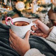 person holding christmas mug with tea and candy cane by tree