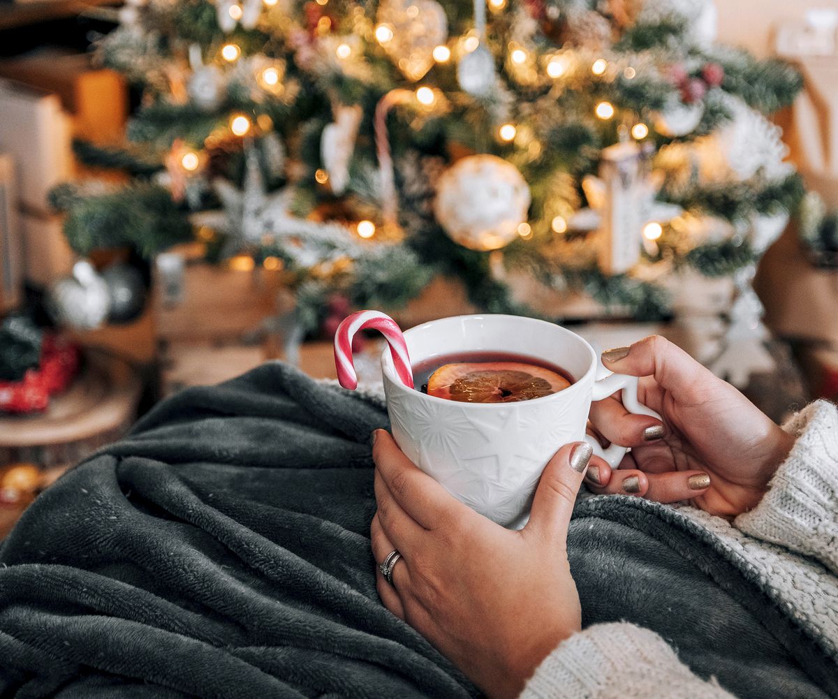person holding christmas mug with tea and candy cane by tree