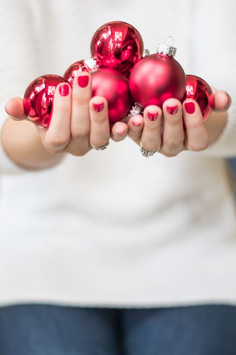 woman holding up red holiday glass christmas ornaments while wearing a white sweater