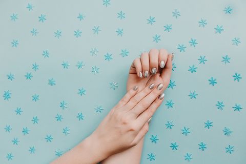 female hands with silver manicure on blue background with snowflakes holiday, new year, shiny sparkles