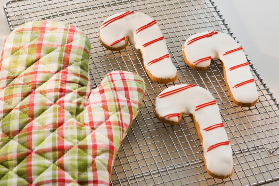 red and green plaid christmas oven mitt next to red and white frosted candy cane cookies cooling on a baking rack