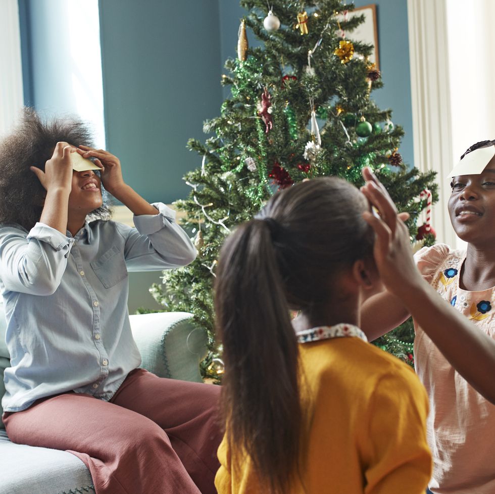 christmas party, sisters sticking adhesive notes on forehead while sitting in living room at home during christmas