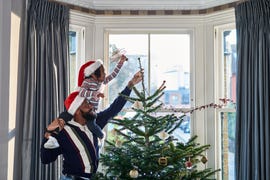 father and daughter decorating christmas tree in bay window at home