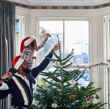 father and daughter decorating christmas tree in bay window at home