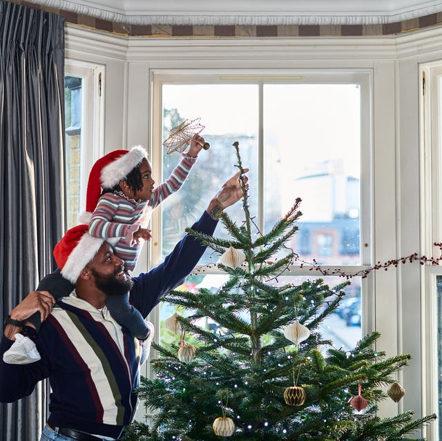 father and daughter decorating christmas tree in bay window at home