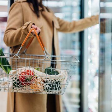 close up shot of woman carrying shopping basket and shopping groceries in supermarket