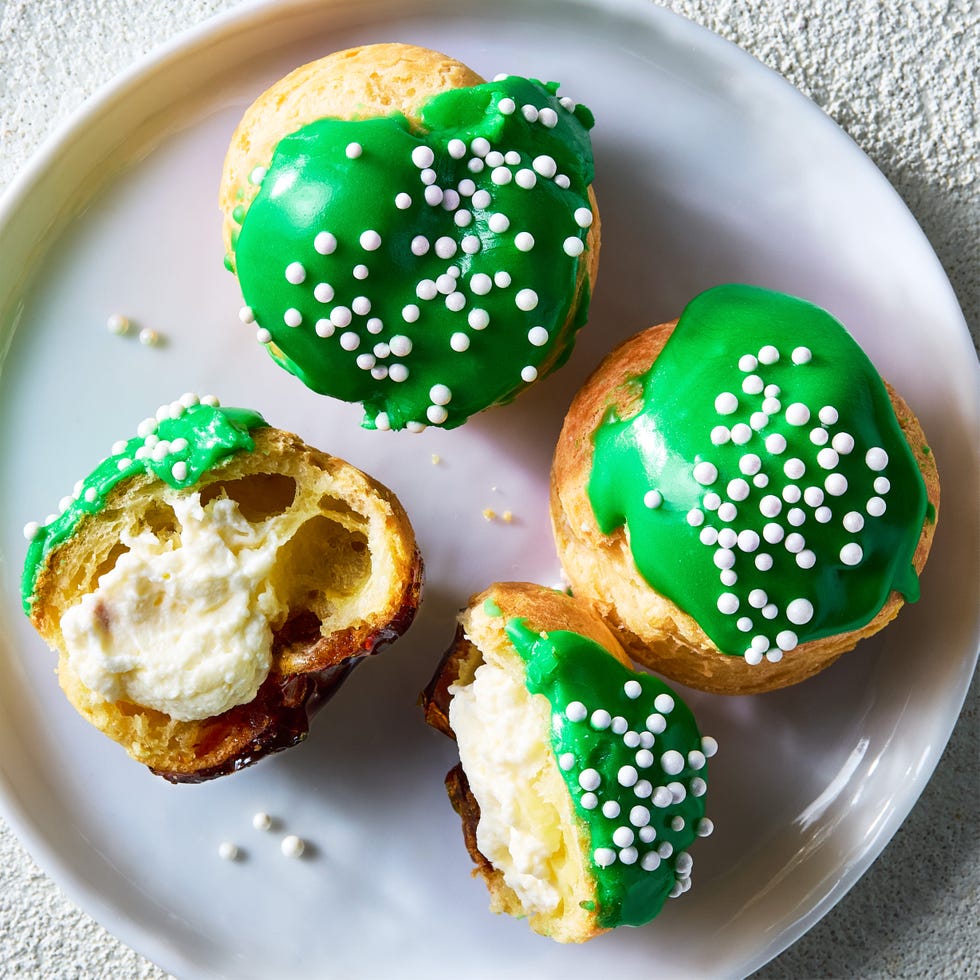 croquembouche in the shape of a christmas tree with green icing and white sprinkles with a sugar cookie star on top