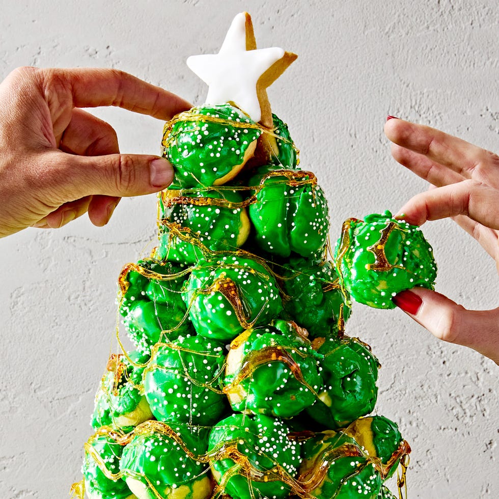 croquembouche in the shape of a christmas tree with green icing and white sprinkles with a sugar cookie star on top