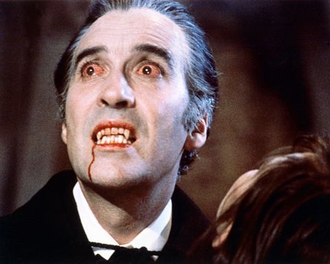 a promotional image of christopher lee from the film dracula, with white face makeup, bloodshot eyes, fangs, and blood dripping down his chin