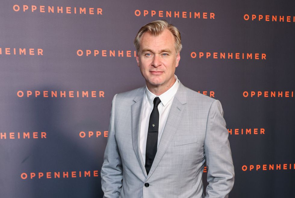 Christopher Nolan, ein Mann steht mit den Händen in den Hosentaschen, er trägt einen grauen Anzug