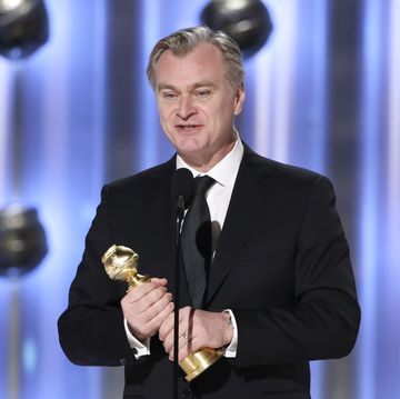 christopher nolan dressed in a dark suit and tie accepts an award on stage at the golden globes 2024