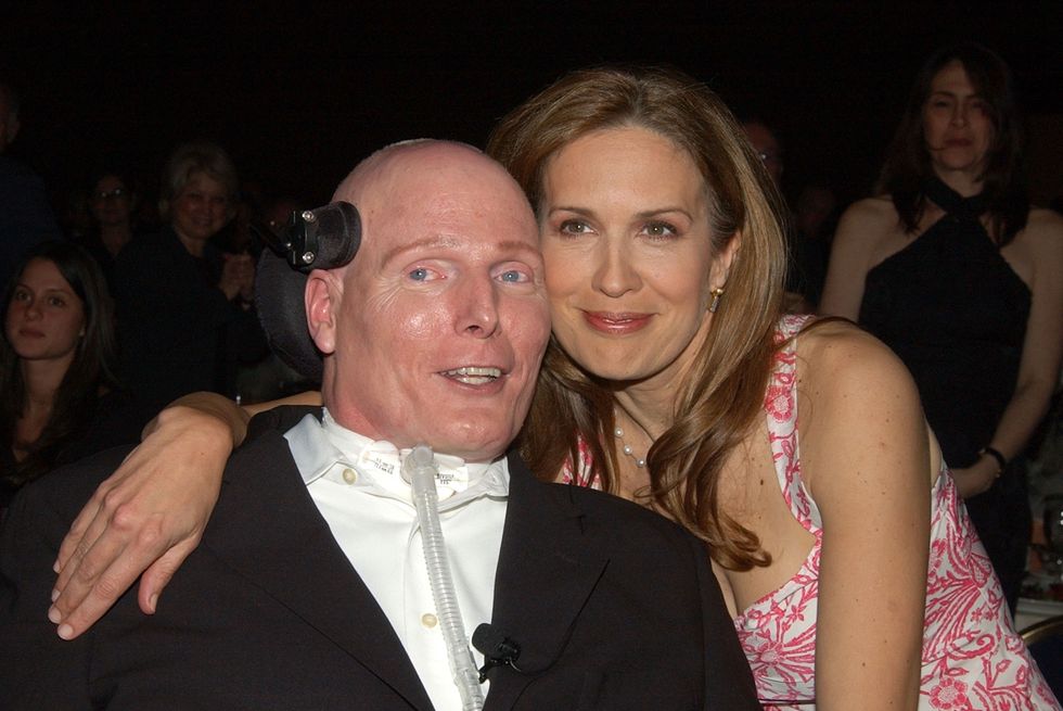 a woman hugs a man in a wheelchair on her right as both smile