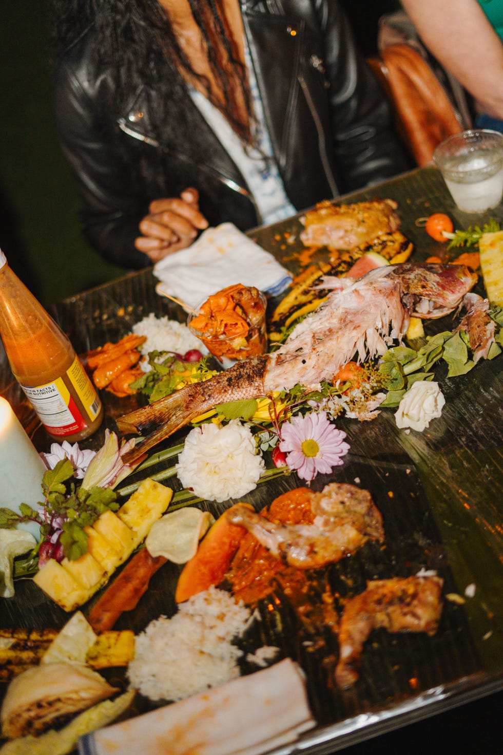 a variety of food served on a large leaf including fish vegetables and flowers