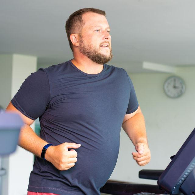 chubby man walking on running track, warming up on gym treadmill