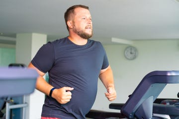 chubby man walking on running track, warming up on gym treadmill