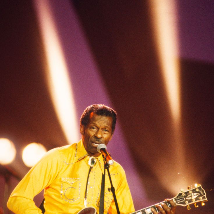 chuck berry holding a guitar as he sings standing behind a microphone