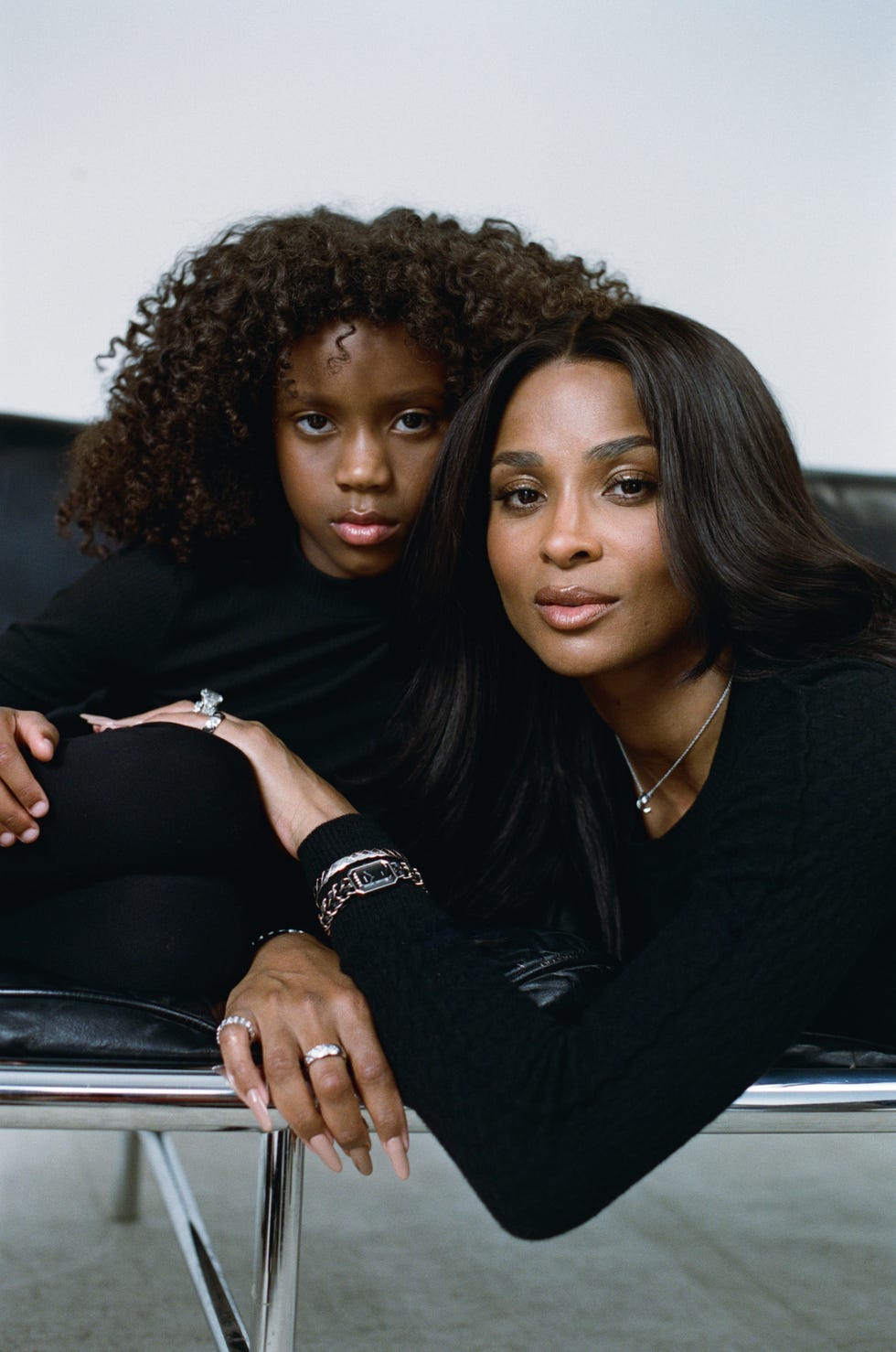 two individuals lounging on a black leather couch dressed in black attire