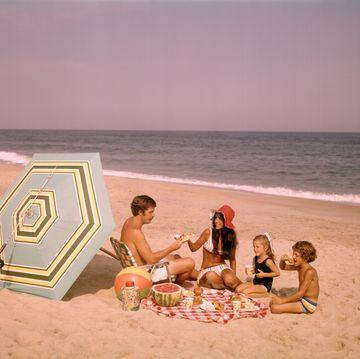 1970s family of four sitting together on ocean seashore by beach umbrella picnicking eating watermelon photo by d corsonclassicstockgetty images