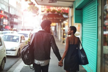 a couple from the back holding hands in a sun dappled city