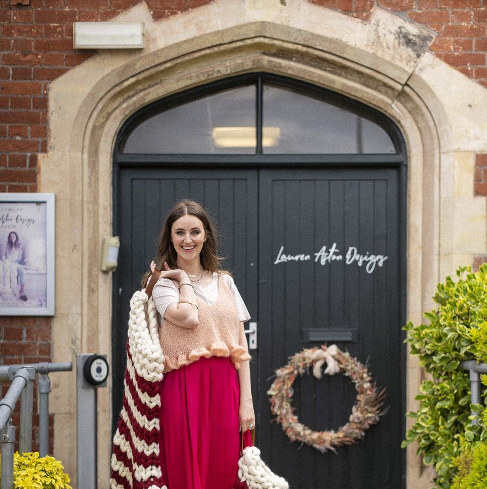 lauren aston designs in south devon, showing off her bestselling christmas knits, christmas stockings, tree oppers, and santa hats, lauren in front of her shop holding two large knit stockings