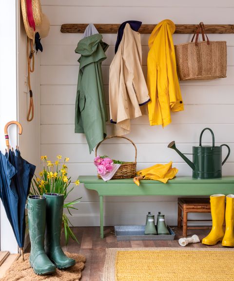 mudroom vignette with raincoats, boots, bench, and watering can