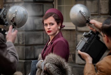 claire foy as margaret campbell in a very british scandal, wearing a burgundy jacket and hat with fur coat and is being photographed by paparazzi