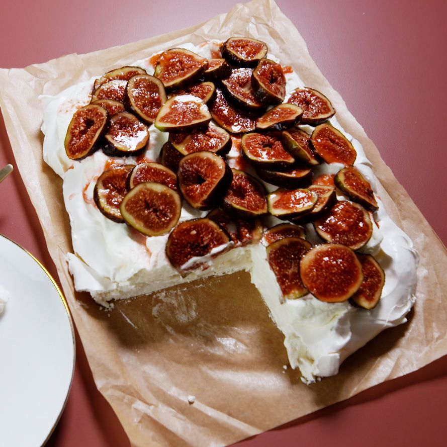 pavlova covered with macerated figs and homemade whipped cream on parchment paper on a red background