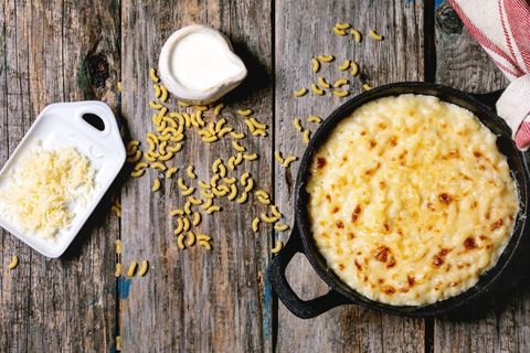 classic american dish baked mac and cheese in cast iron pan with kitchen towel and ingredients above over old wooden background