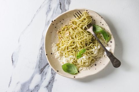 Classic italian spaghetti pasta with pesto sauce, pine nuts, olive oil and fresh basil. Served in ceramic plate with fork over white marble background. Flat lay, space